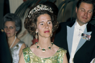 Koningin Fabiola kijkt peinzend in galajurk met groen patroon en draagt de oorbellen en het collier