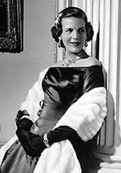 Prinses Lilian in zwarte avondjurk en witte bontstola leunt glimlachend tegen een pilaar in het paleis